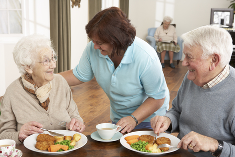 Älteres Paar bekommt von Betreuer eine Mahlzeit serviert.